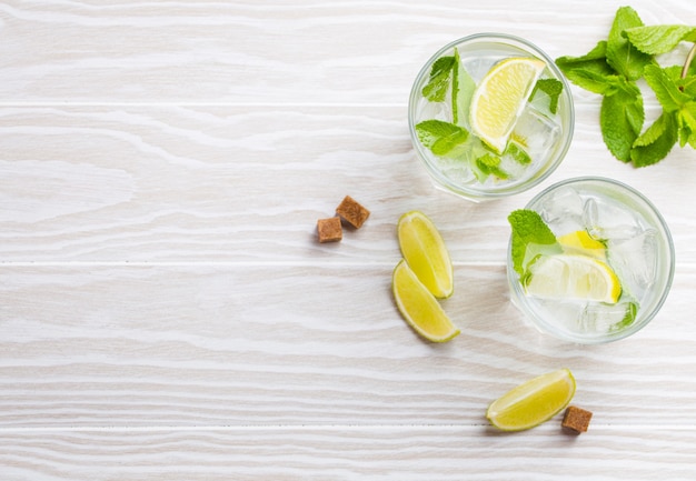 Zomerdrankjes met ijs, schijfjes limoen, verse munt in glazen op witte houten rustieke achtergrond, ruimte voor tekst. Koude verfrissende limonades/mojito geweldig voor zomerfeest en plezier, kopieer ruimte, bovenaanzicht