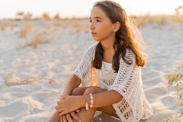 Zomerfoto van een klein meisje in een stijlvolle boho-outfit die op het strand poseert warme zonsondergangkleuren wacation en reisconcept