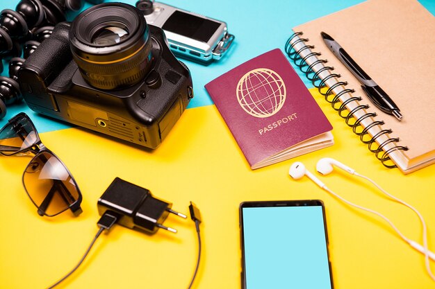 Zomerfotograafkit die graag reist op een tweekleurige achtergrond. DSLR en actiecamera naast andere accessoires, smartphone, oplader en paspoort