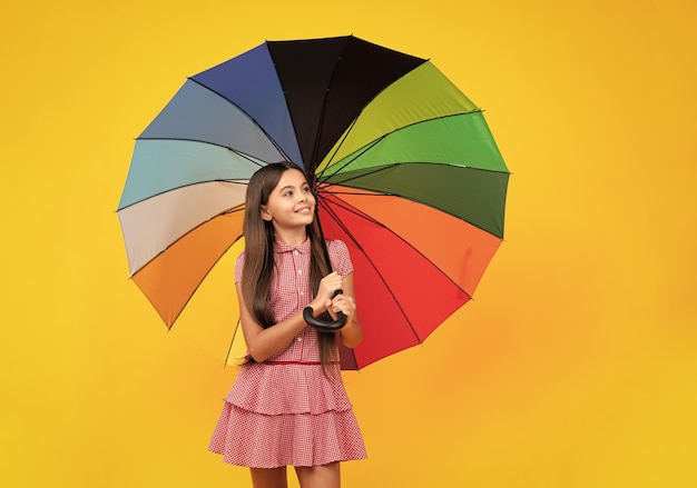 Zomerjurk Gelukkig tienermeisje met regenboog paraplu staande geïsoleerd op gele achtergrond geïsoleerd op wit Vrolijke tiener kind houd parasol