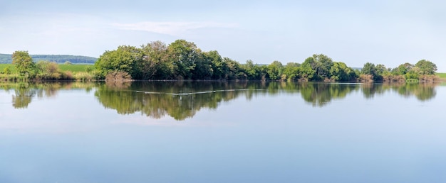 Zomerlandschapspanorama met rivier en bomen weerspiegeld in rivierwater