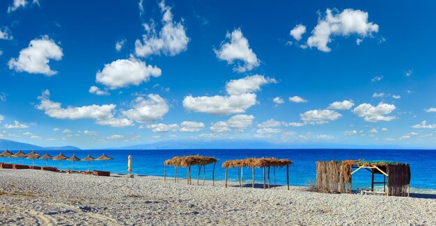 Zomerochtend strand met ligbedden luifels en witte kiezelsteen Borsh Albanië Diepblauwe lucht met wat wolken Drie schoten stitch panorama