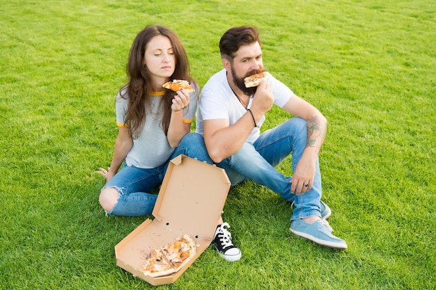 Zomerpicknick gemakkelijke en snelle ideeën Fastfood Bebaarde man en vrouw genieten van goedkope pizza Paar verliefd buitenshuis daten met pizza Hongerige studenten eten delen Paar pizza eten ontspannen op gazon