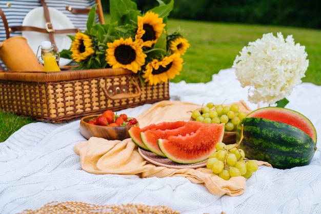 Zomerpicknickconcept op zonnige dag met watermeloen, fruit, boekethortensia en zonnebloemenbloemen.