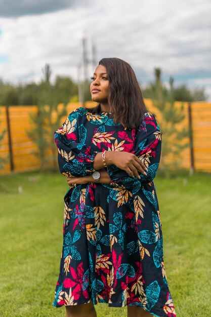 Zomers portret van een mooie afro-amerikaanse vrouw in een kleurrijke kledingslijtage die op de achtertuin staat