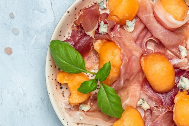 Zomers voorgerecht met zoete meloen en prosciutto en basilicum Antipasti Traditioneel Spaans en Italiaans voorgerecht Bovenaanzicht op witte stenen tafel Lang bannerformaat bovenaanzicht