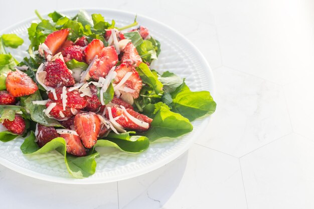 Zomersalade met aardbeien op een witte plaat en een lichte achtergrond Close-up plaats voor kopieerruimte