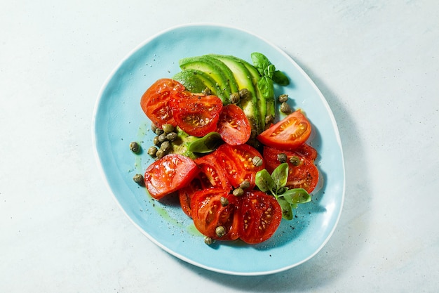 Zomersalade met rijpe tomaten en avocado met kappertjes in een blauw bord op tafel