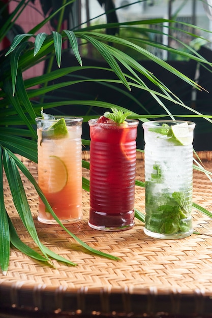 Zomerse gekoelde drankjes met vers sap, mochito, hibiscus, mango op rieten tafel met bladeren