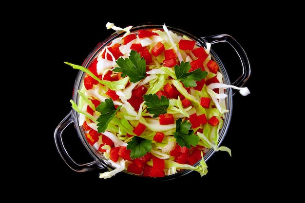 Zomerse salade lichte snack voor een picknick van witte kool en paprika met peterselie in een glazen kom geïsoleerd op een zwarte achtergrond