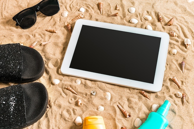 Zomerslippers, tablet, zonnebril en zeeschelp op zand. Met plaats voor uw tekst. Bovenaanzicht