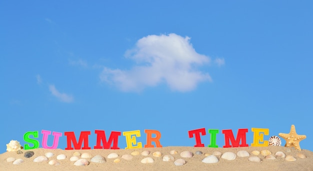 Zomertijd letters op een strand zand tegen de blauwe lucht