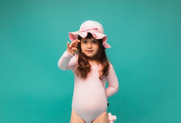 Zomervakantie aan zee vrolijk meisje in een roze zwempak en een hoed op een turquoise achtergrond Plaats voor tekst van hoge kwaliteit foto