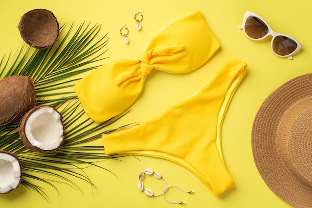 Zomervakantie concept Bovenaanzicht foto van gele bikini hoed stijlvolle zonnebril schelp armband oorbellen kokosnoten en palmbladeren op geïsoleerde gele achtergrond