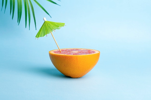 Zomervakantie concept. Grapefruit met een cocktailparaplu op een gekleurde achtergrond. Tropen, zon, strand, vitamines, fruit, zomer en goed humeur