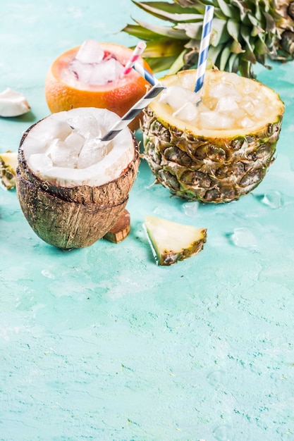 Zomervakantie drankje concept, stel verschillende tropische cocktails of sappen in ananas, grapefruit en kokosnoot met ijs, lichtblauw beton