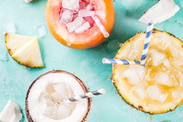 Zomervakantie drankje concept, stel verschillende tropische cocktails of sappen in ananas, grapefruit en kokosnoot met ijs, lichtblauw beton