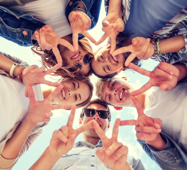 Foto zomervakantie en tienerconcept - groep tieners die vrede of overwinningsgebaar tonen