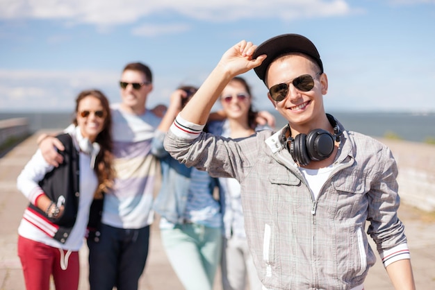 zomervakantie en tienerconcept - tiener in zonnebril, pet en koptelefoon die buiten met vrienden rondhangt