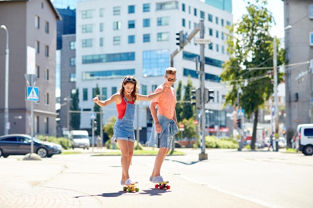 zomervakantie, extreme sport en mensenconcept - gelukkig tienerpaar dat korte moderne cruiser-skateboards berijdt op straat in de stad