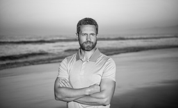 Zomervakantie knappe man met baard in zonsondergang over zee ongeschoren man op ochtend strand lachende blanke man op zonsopgang strand bebaarde man in shirt zomer mode stijl