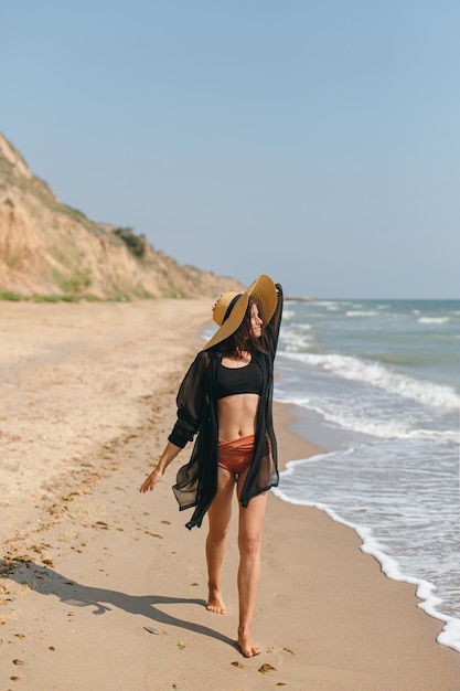 Zomervakantie Mooie stijlvolle vrouw met hoed wandelen op zandstrand op zee golven en ontspannen