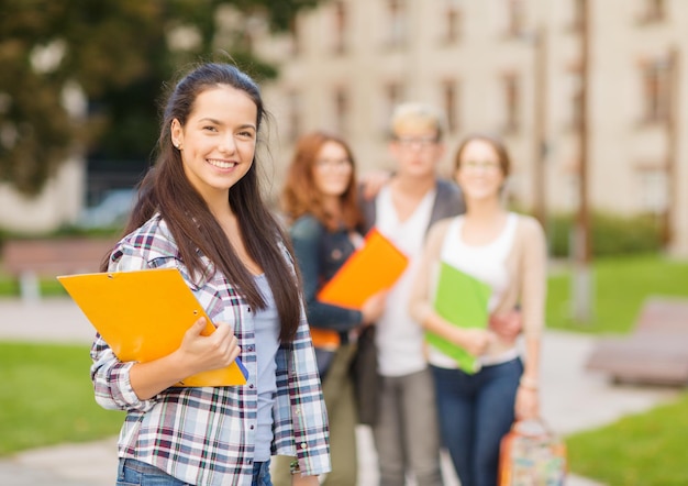 zomervakantie, onderwijs, campus en tienerconcept - glimlachende vrouwelijke student met mappen en groep achterin