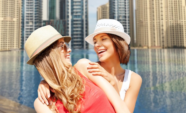 zomervakantie, reizen, mensen en vakantieconcept - gelukkige jonge vrouwen in hoeden over infinity edge pool op de achtergrond van dubai