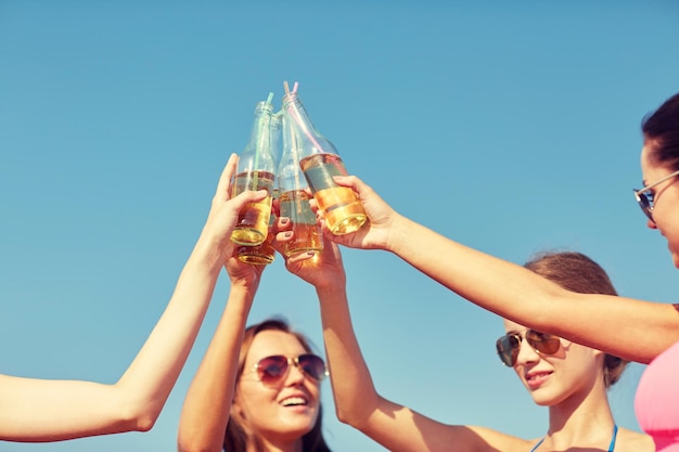 zomervakantie, vakantie, feest, reizen en mensen concept - close-up van gelukkige jonge vrouwen met drankjes rammelende flessen