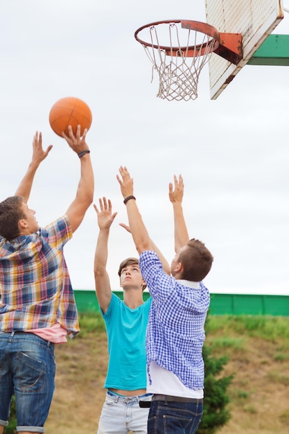 zomervakantie, vakantie, games en vriendschapsconcept - groep tieners die buiten basketbal speelt