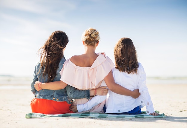 zomervakantie, vakantie, reizen en mensen concept - groep jonge vrouwen in casual kleding knuffelen zittend op stranddeken