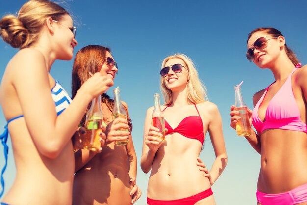 zomervakantie, vakantie, reizen en mensen concept - groep lachende jonge vrouwen zonnebaden en drinken op het strand