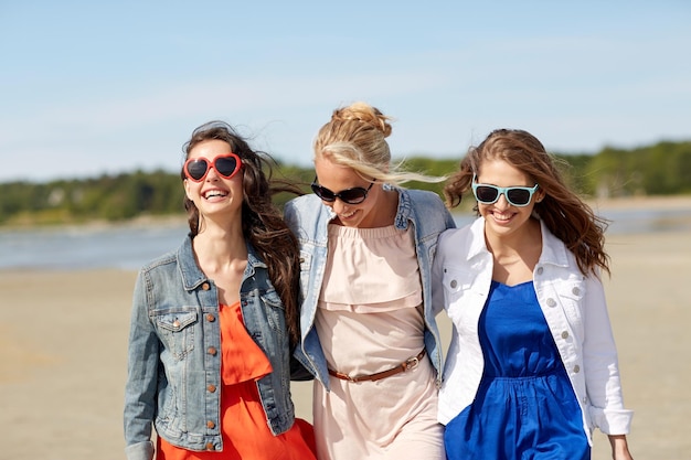 zomervakantie, vakantie, reizen en mensenconcept - groep glimlachende jonge vrouwen in zonnebrillen en vrijetijdskleding op het strand