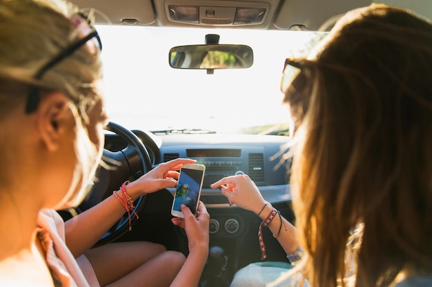 zomervakantie, vakantie, reizen, roadtrip en mensenconcept - gelukkige tienermeisjes of jonge vrouwen met smartphone die selfie in de auto nemen