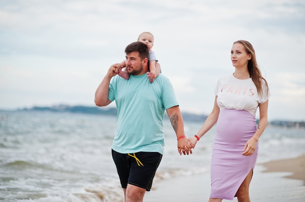 Zomervakanties. Ouders en mensen buitenactiviteit met kinderen. Fijne familievakanties. Vader, zwangere moeder, dochtertje op zee zandstrand.