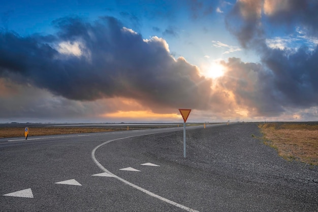 Zon schijnt door wolken over lege weg tegen hemel tijdens zonsondergang