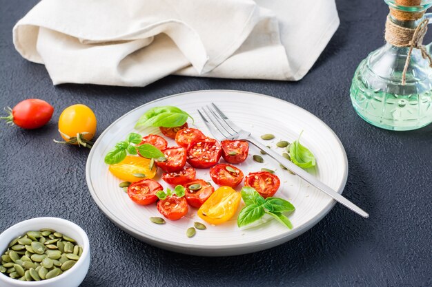 Zongedroogde tomaten met basilicum, sesamzaadjes en pompoen op een bord op een zwarte achtergrond. Vegetarisch eten