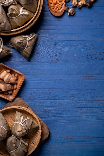 Концепция фестиваля лодок-драконов Zongzi Рисовые клецки традиционной китайской кухни на синем деревянном фоне для фестиваля Duanwu, вид сверху, концепция плоской планировки