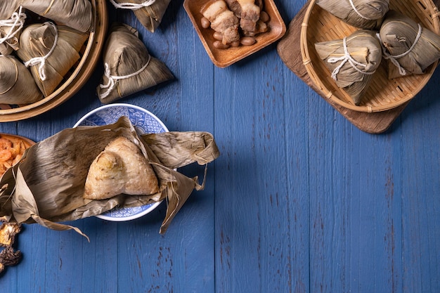 Концепция фестиваля лодок-драконов Zongzi Рисовые клецки традиционной китайской кухни на синем деревянном фоне для фестиваля Duanwu, вид сверху, концепция дизайна плоской планировки