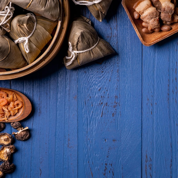 Концепция фестиваля лодок-драконов Zongzi Рисовые клецки традиционной китайской кухни на синем деревянном фоне для фестиваля Duanwu, вид сверху, концепция плоской планировки