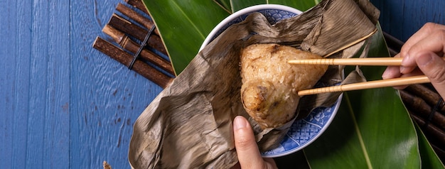 Концепция фестиваля лодок-драконов Zongzi Рисовые клецки традиционной китайской кухни на синем деревянном фоне для фестиваля Duanwu, вид сверху, концепция плоской планировки