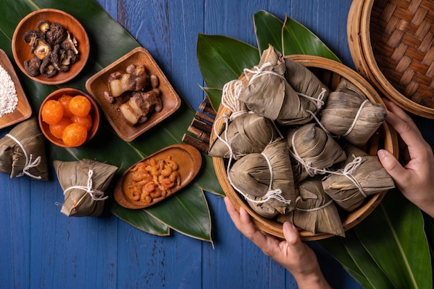 Концепция фестиваля лодок-драконов Zongzi Рисовые клецки традиционной китайской кухни на синем деревянном фоне для фестиваля Duanwu, вид сверху, концепция плоской планировки