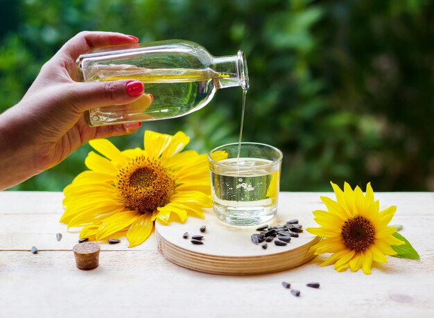 Zonnebloemolie giet uit de fles in een glas met zonnebloemen en zaden op de achtergrond