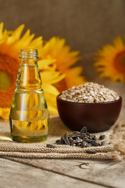 Zonnebloemolie in een glazen fles met zaden in een beker en bloemen