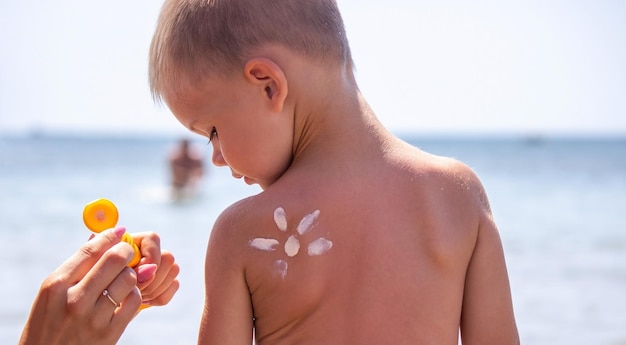 Zonnebrandcrème op het gezicht en de rug van het kind Op de achtergrond van de zee