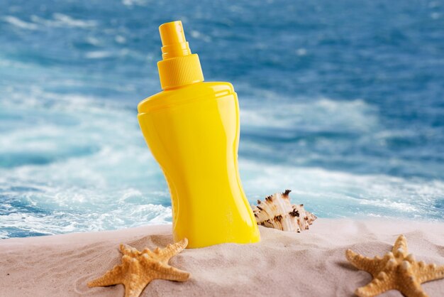 Foto zonnebrandcrème spray fles op een zandstrand versierd met verschillende schelpen tegen de achtergrond van zee golven