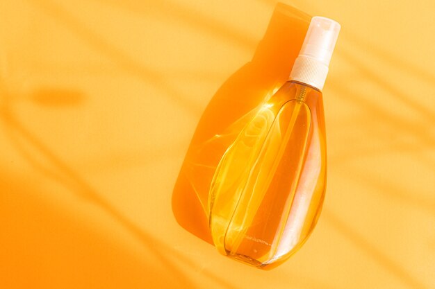 Zonnebrandolie in een plastic spuitfles op oranje achtergrond en zonneschaduw