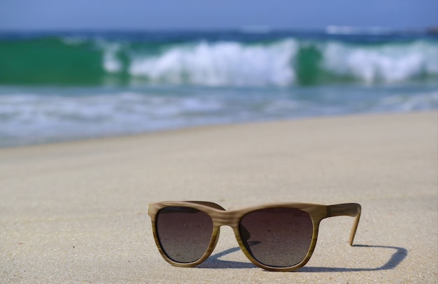 Zonnebril op het strand met wazig spatten golven