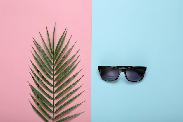 Zonnebrillen en palmbladeren op roze blauwe achtergrond Tropische minimale lay-out Bovenaanzicht Plat leggen
