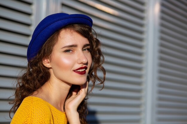 Zonnig portret van aantrekkelijk meisje met Bourgondische lippenstift met blauwe hoed. Ruimte voor tekst